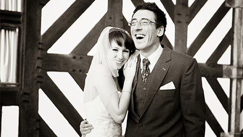 Bride and Groom cuddle and laugh for the wedding photographer outside the striking black and white tudor style wall at the Hillbark Hotel in the Wirral