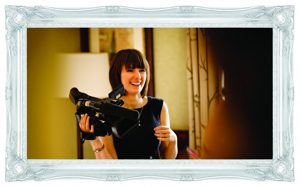 a female wedding videographer holds her sony video camera and laughs towards someone off screen. Photo taken by Mick Cookson Photography