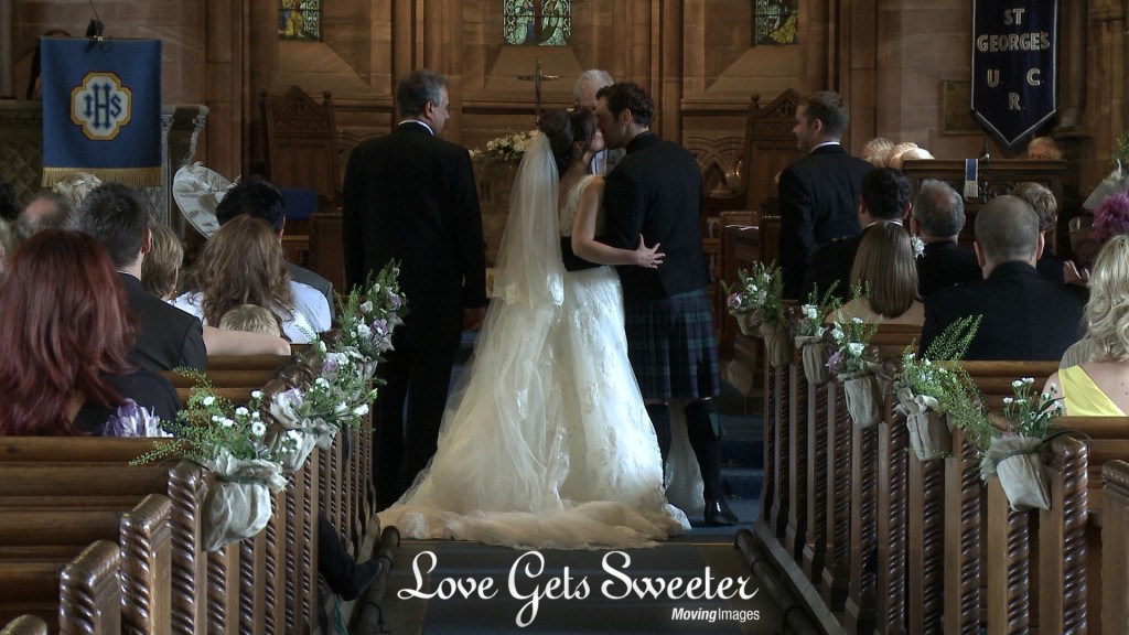 A videographer still of the bride and groom enjoy a kiss as the priest announces them as husband and wife at St Georges Church in Thornton Hough in the Wirral