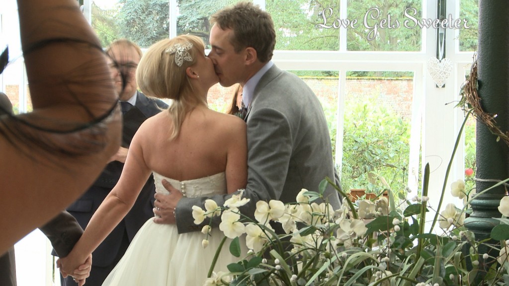 Liam the Groom gives his wife to be a huge kiss as she meets him at the bottom of the aisle in the glasshouse at Combermere abbey before their wedding ceremony starts