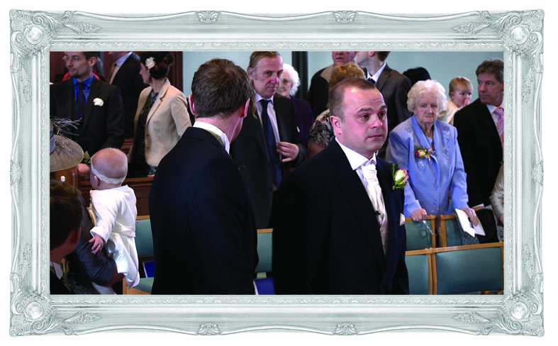a wedding video still of a nervous groom waiting inside St John's Church in Burscough as his bride walks down the aisle