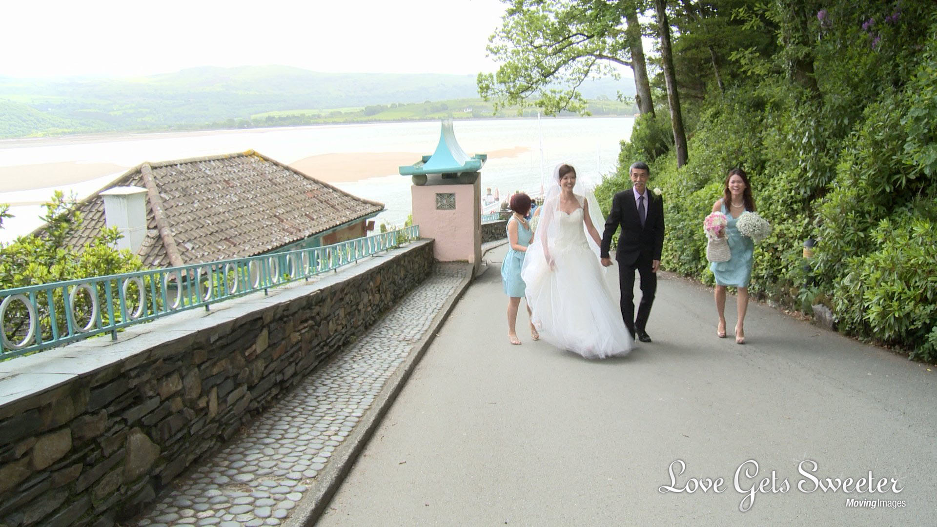 a bride and her two bridesmaids wearing mint green walk up the hill at portmeirion towards the ceremony room being filmed by the wedding videographer Love Gets Sweeter