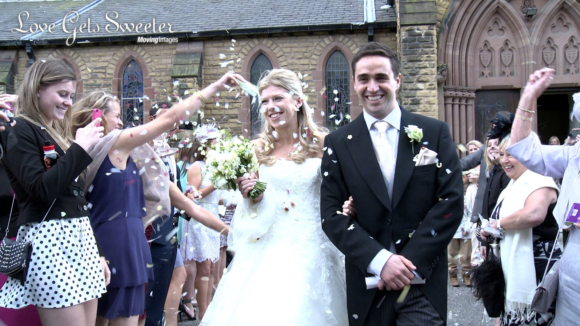 a bride and groom smile sweetly as they walk away from St Joseph;s Church and towards their wedding videographer whilst being showered in white confetti