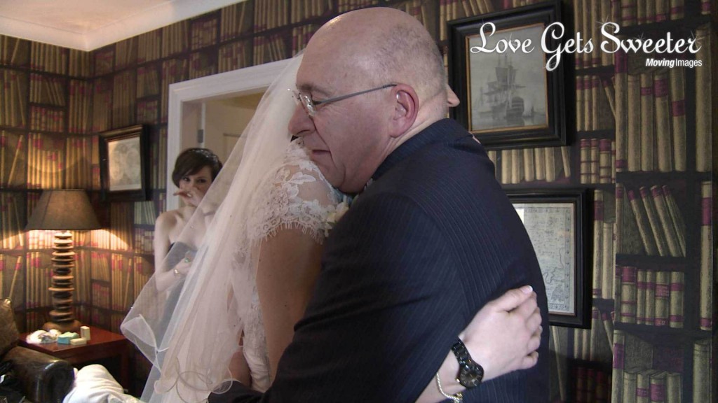 A video still of A father of the bride gives his daughter an emotional bear hug with tears in his eyes as he sees her for the first time before she gets married at Mitton Hall