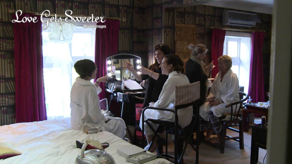 Phoebe at Flossy and Leigh laughs and chats with the bride and maid of honour as they have their hair and make-up done for a wedding at Mitton Hall