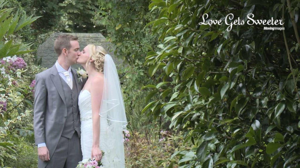 A video still of Mike and Michelle the bride and groom kiss under the archway in the gardens of Abbeywood Estate in Delemere Forest