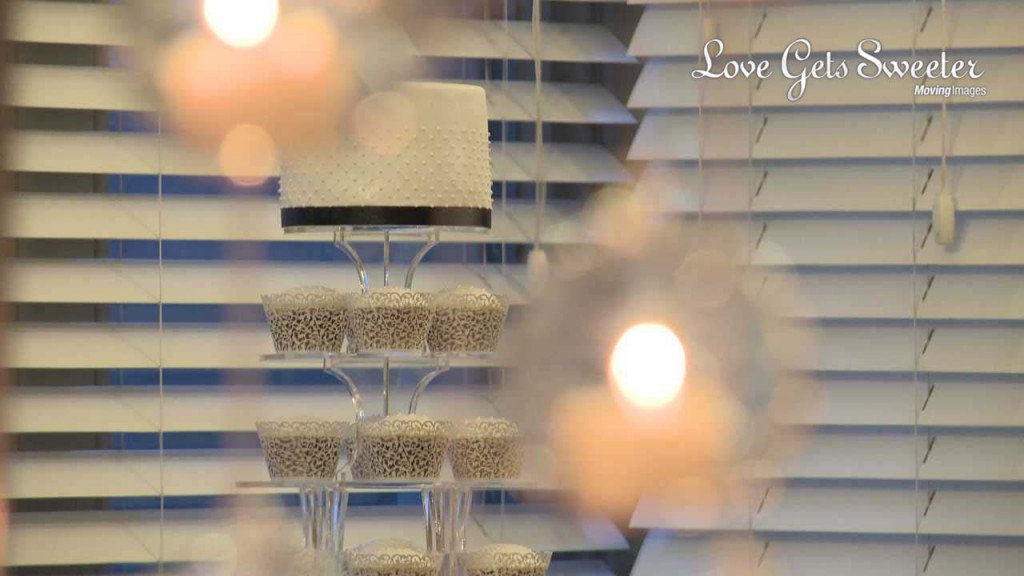 A cup cake tower and classic white wedding cake with navy ribbon hiding behind hanging candle pendants creating a romantic look