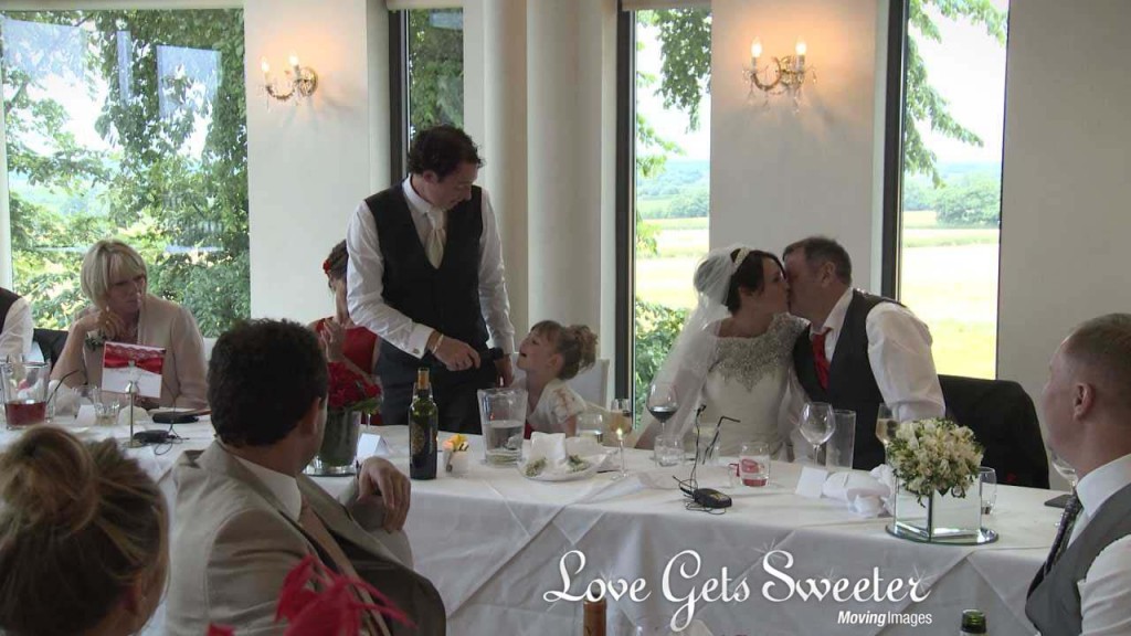 A wedding videographer films The bride gives her dad a kiss after his speech as they sit at the top table during the wedding speeches at The West Tower in Aughton near Ormskirk