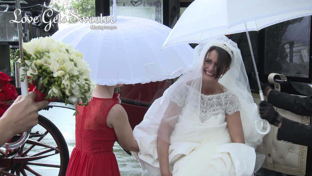 a wedding video still of A bride steps out of her carriage laughing in the rain as her bridesmaids try to hold umbrellas over her head outside her church in Dalton