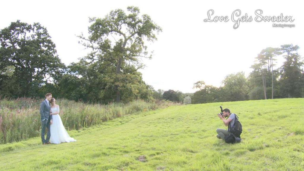 a video still of Mr Sleeve wedding photographer crouching down in the grass to get a beautiful wedding photo of the bride and groom in the grounds at Rookery Hall