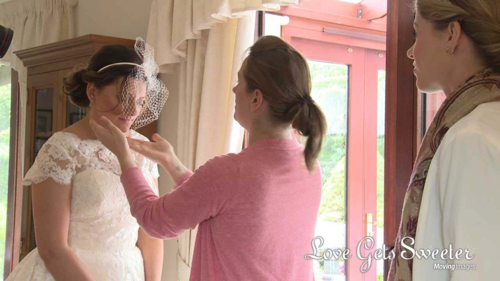 A wedding video still of Michelle Sisson helping a bride getting ready and having her vintage inspired birdcage veil adjusted before her wedding at Soughton Hall