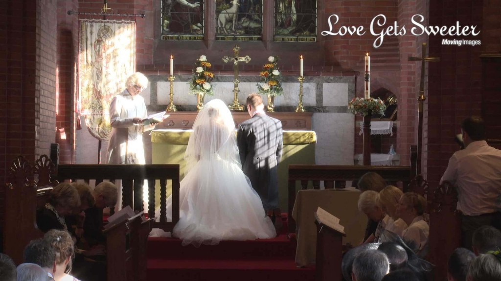 a bride and groom kneel at the alter during their wedding blessing at St John's Church in High Legh Cheshire and the wedding videographer films from the back as the sun shines down on them beautifully