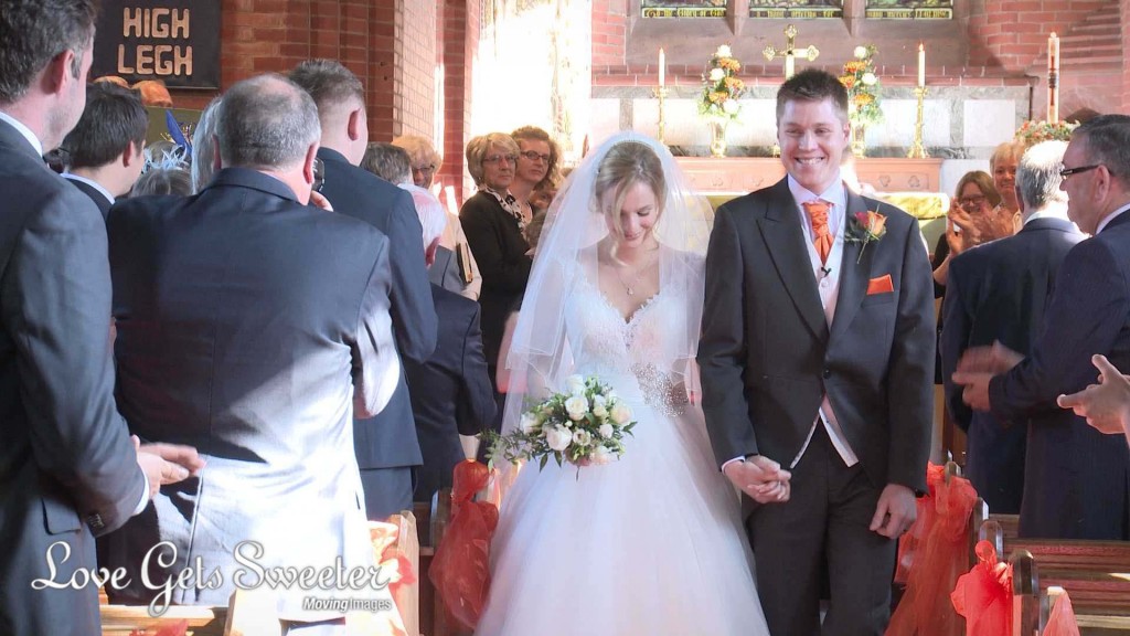 the shy bride looks down as the groom smile is wide. They walk down the aisle at St Johns in High Legh towards their wedding videographer Love Gets Sweeter
