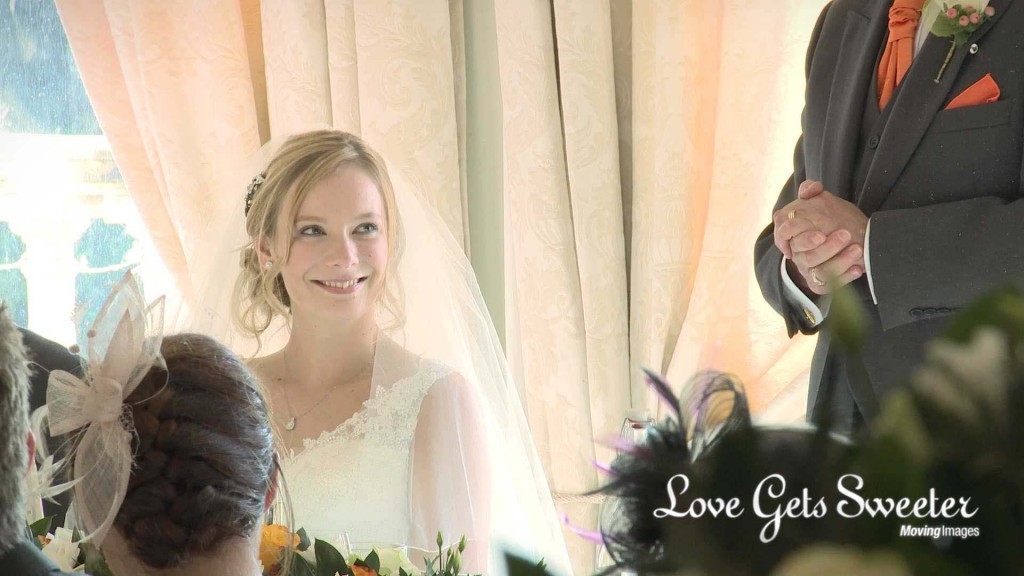 a close up on the wedding video of the bride smiling as she sits and listens to her dad during his wedding speech at willington hall