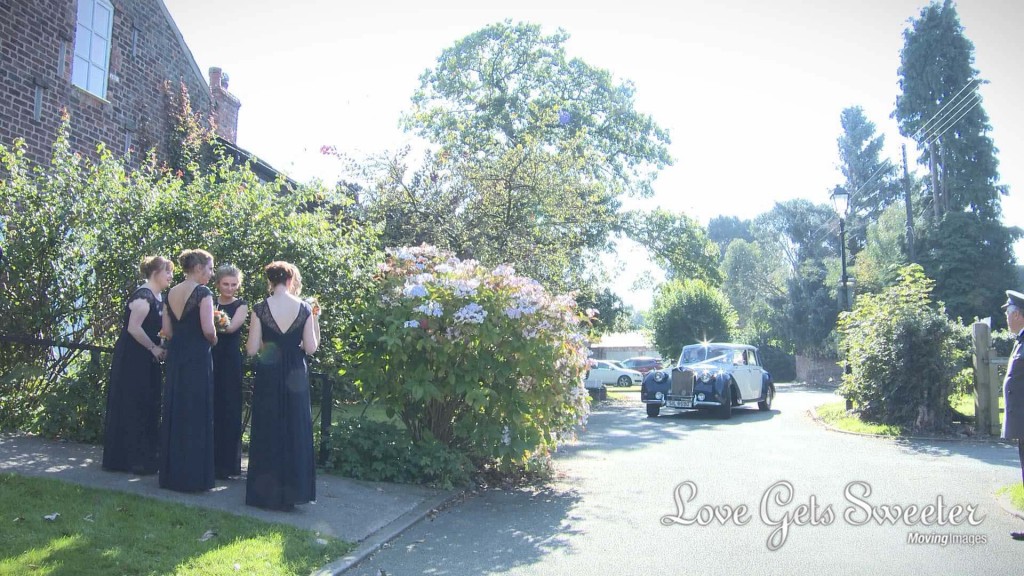 the bridesmaids in their floor length navy bridesmaid dresses wait on the path to the church as the navy and blue 'emma' Horgans wedding car comes round the corner with the bride and her Dad as the wedding videographer waits