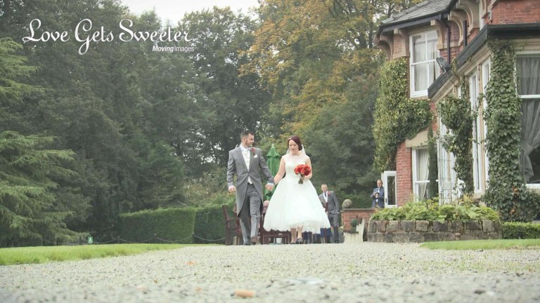 bride and groom walking around gardens at Bartle Hall and shes holding a red and orange bridal bouquet wearing a tea length dress for their winter wedding in Lancashire