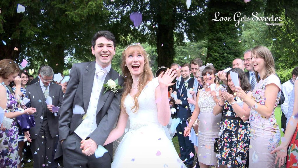 the bride and groom pose covered in purple heart shaped colourful wedding confetti outside mitton hall lancashire
