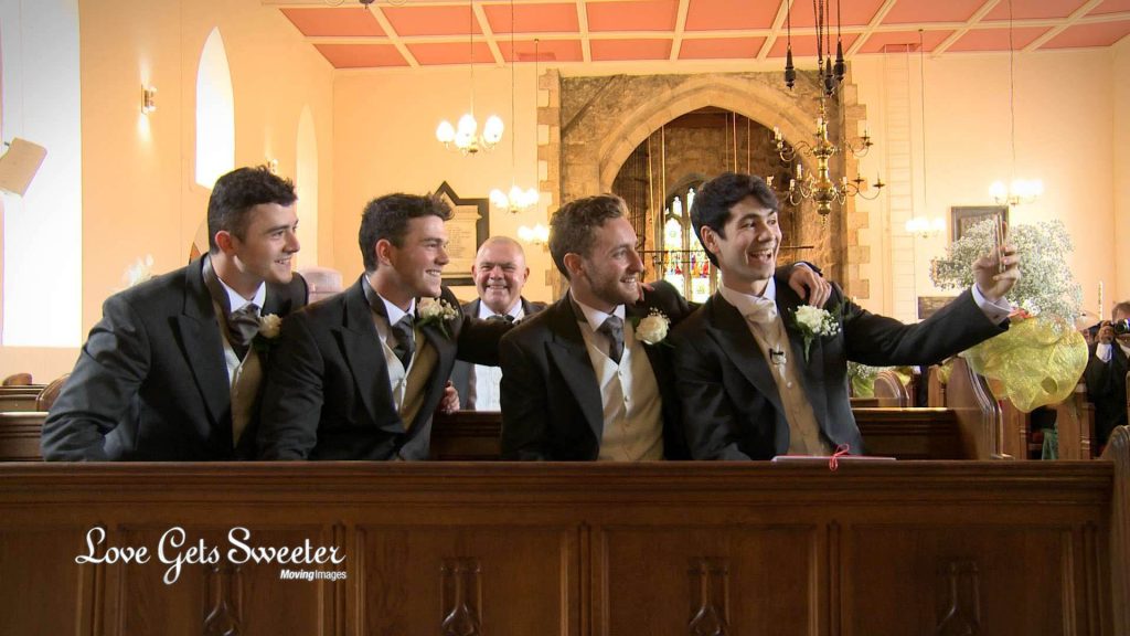 The groom, best man and ushers pose for a selfie sat in the front pew of st johns church in broughton near preston on their wedding video