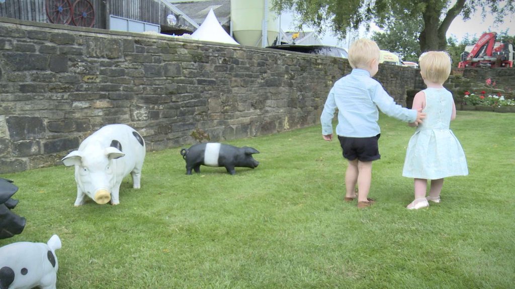cute young boy and girl cuddling up to each other at a wedding surrounded by plastic pigs during a farm wedding