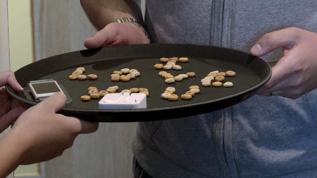 the best man holds a tray with cheerios spelling out I Love You to remind the bride of the grooms romantic proposal before they get married at On The 7th in Media City Salford for their wedding video
