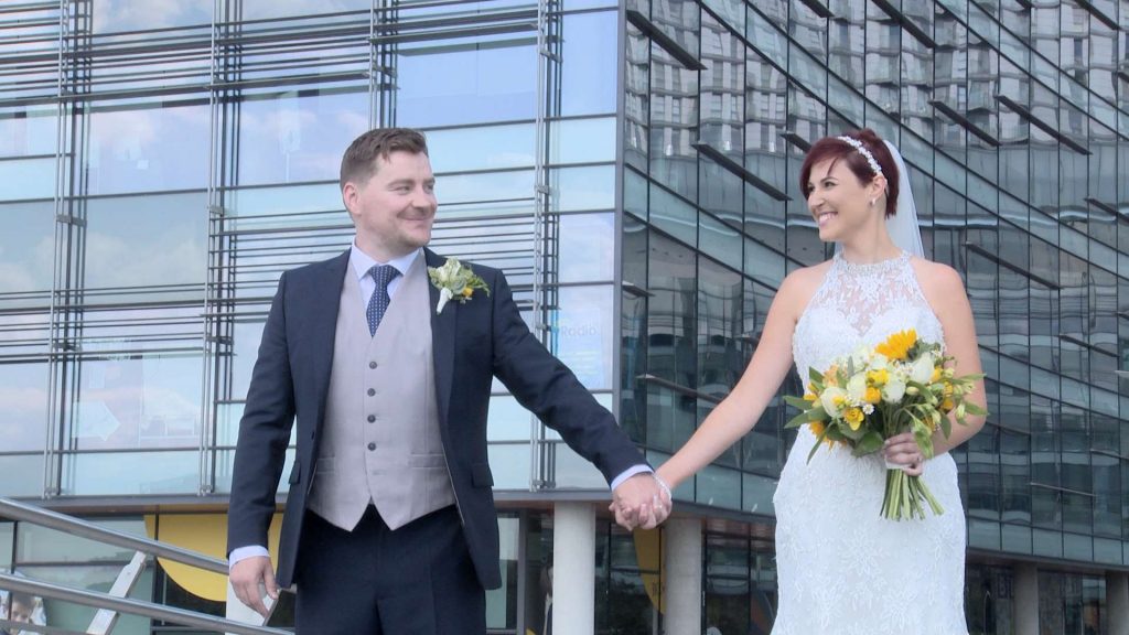 the bride and groom hold hands and look at each other for their wedding photographs at Media City Manchester