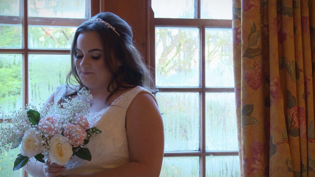 The bride glances at her pretty pink and cream silk bridal flowers bouquet before she gets married on Boxing Day at Nunsmere Hall