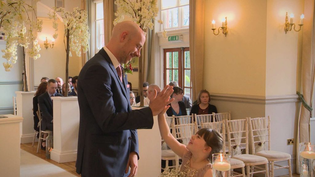 The Groom gives his daughter and flower girl a high five as they wait for the bride to arrive at their wedding ceremony at Nunsmere Hall