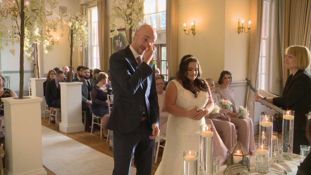 Caught on their wedding video the groom uses a tissue to wipe away his tears after seeing his bride walk down the aisle for their Winter Nunsmere Hall winter wedding