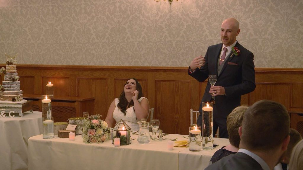the groom makes the bride laugh out loud during his wedding speech on their wedding video the table looks romantic with candles