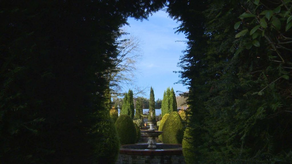a doorway has been created in a manicured hedge in the gardens of Nunsmere Hall to create a perfect frame for a wedding photo