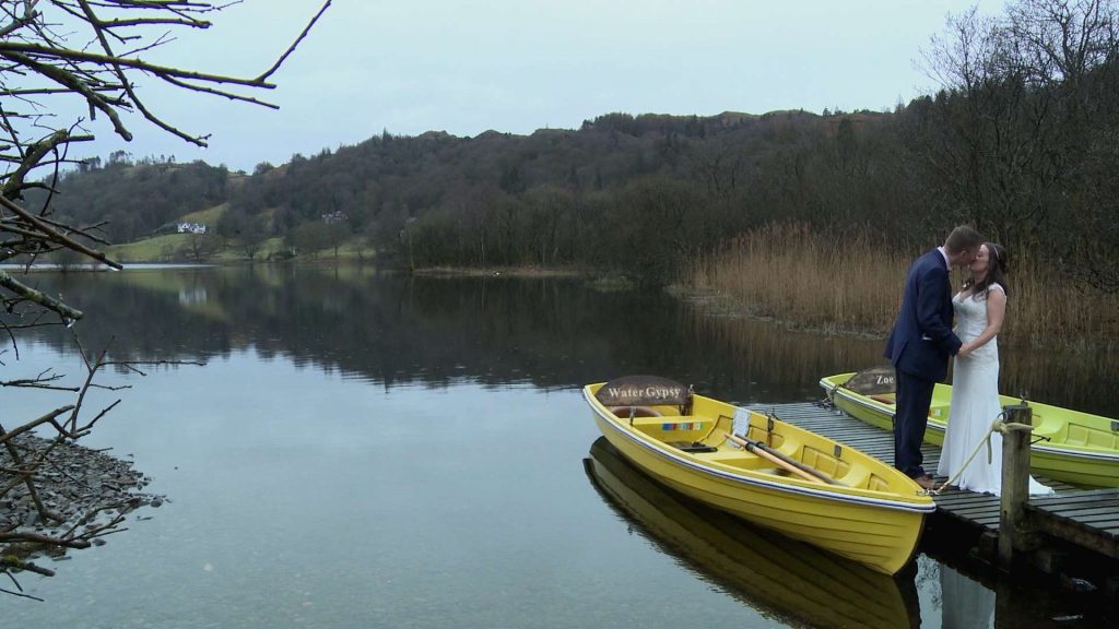 a wide shot of Grasmere lake with a bride and groom standing on the jetty for their wedding photos