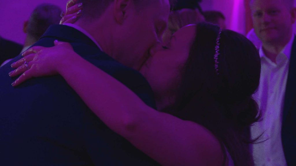 the bride and groom enjoy a kiss on the dance floor under pink lights for their wedding first dance at the wordsworth hotel