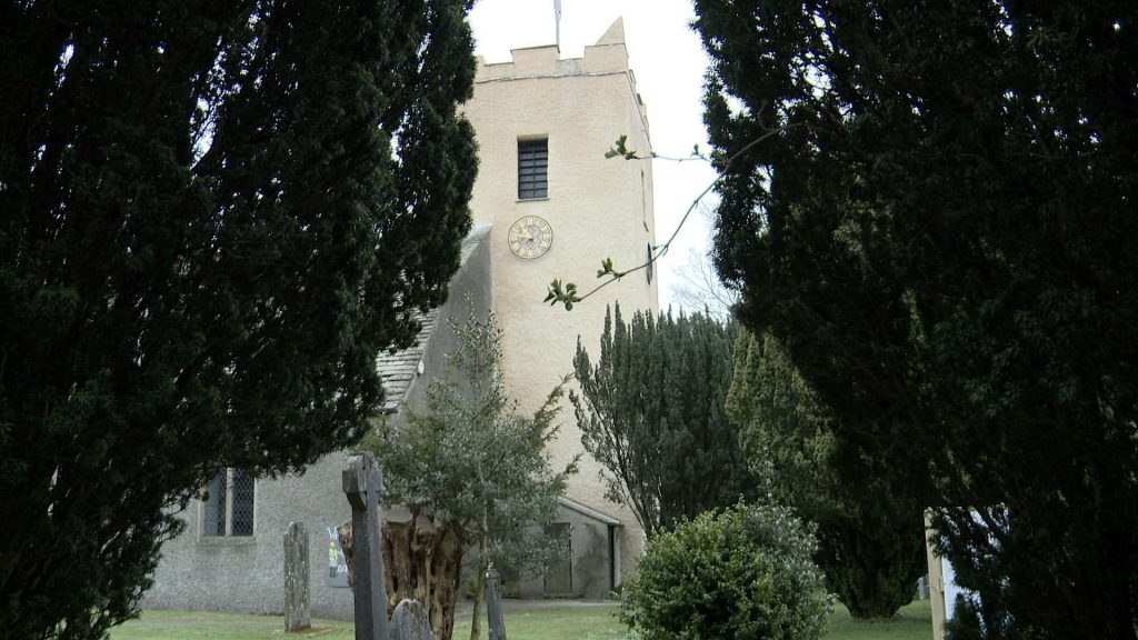the tower of St Oswalds church in grasmere peeking through the rain and trees