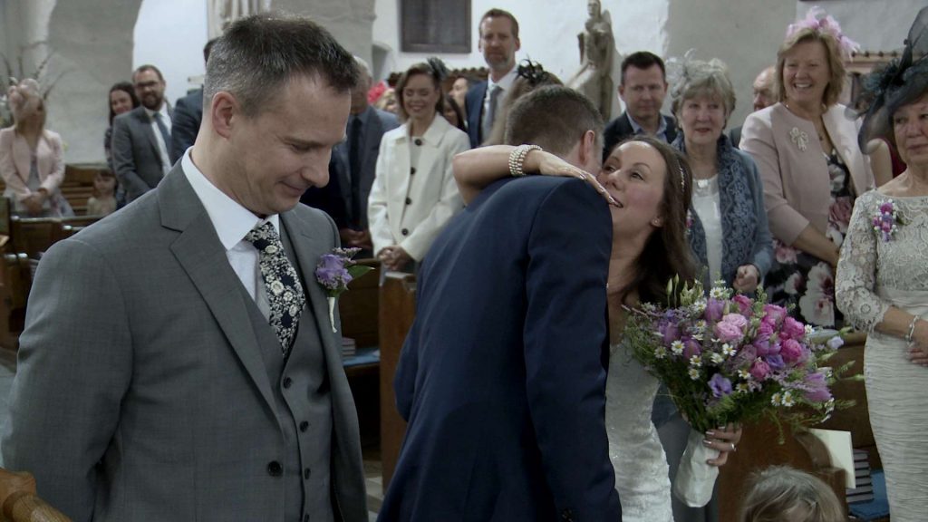 the bride embraces the groom whilst holding her hand tied garden flower bouquet just before they get married in front of their friends and family