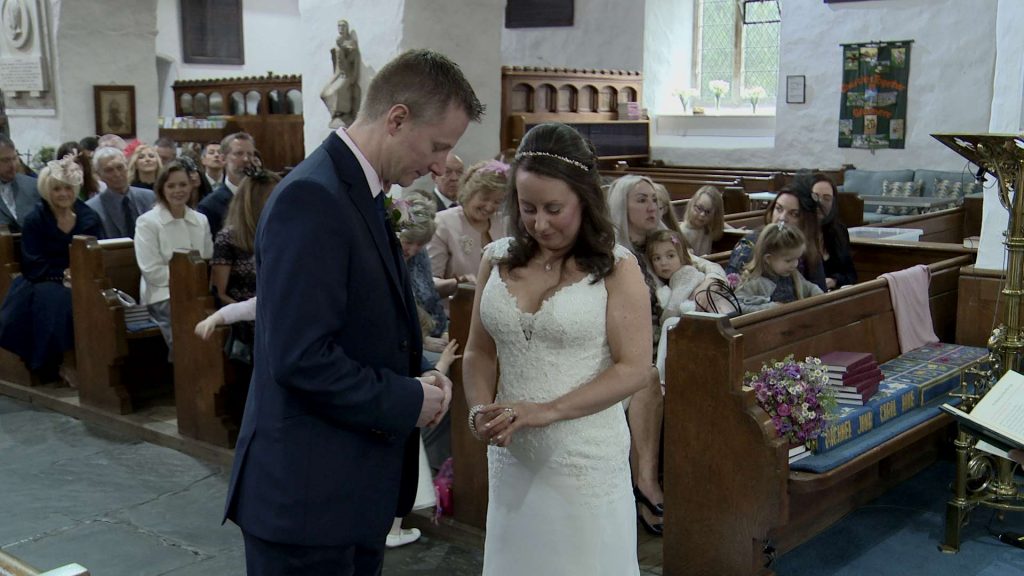 the bride and groom adjust their new wedding rings on their fingers after saying their wedding vows at St Oswalds church in Grasmere