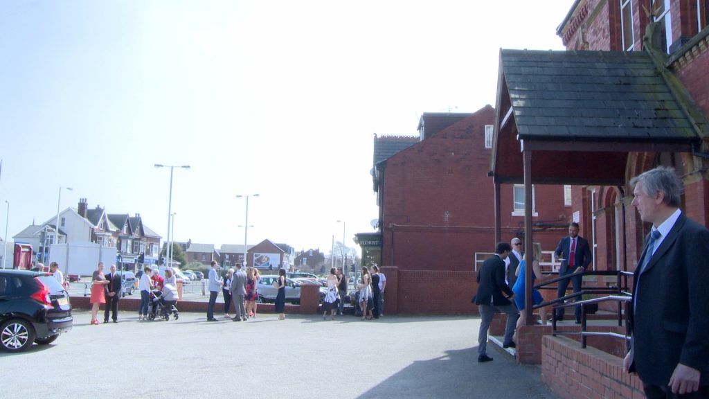 guests stand outside marshside road methodist church in the bright sunsine waiting for the bride to arrive for the wedding