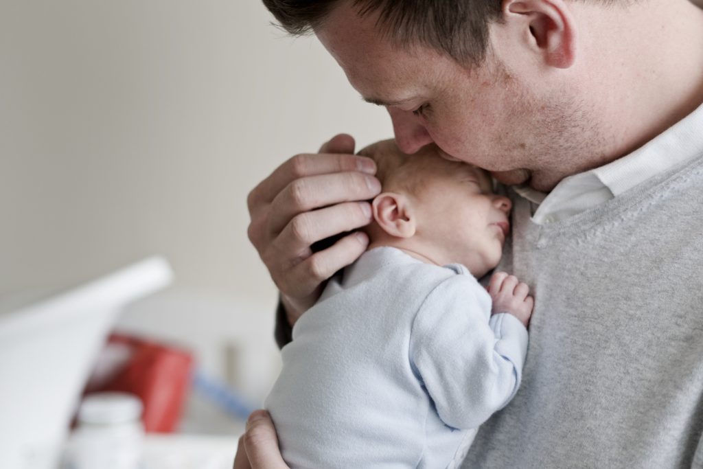 A dad gently kisses his newborn son on the side of the head as he cuddles him