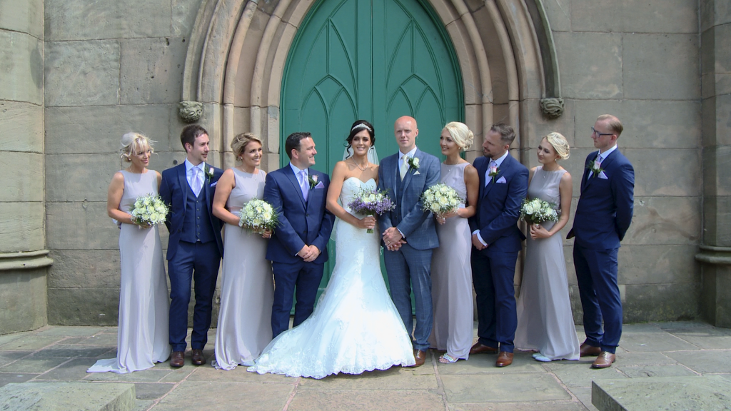 the bridal party pose with the bride and groom in lilac and navy colour scheme holding cream and white bridesmaid bouquets