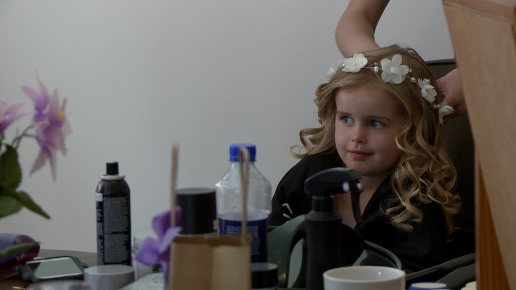 a video still of a young flower girl wearing a white flower crown added to her curled hair by the hair dresser for her Mum's wedding in Burscough