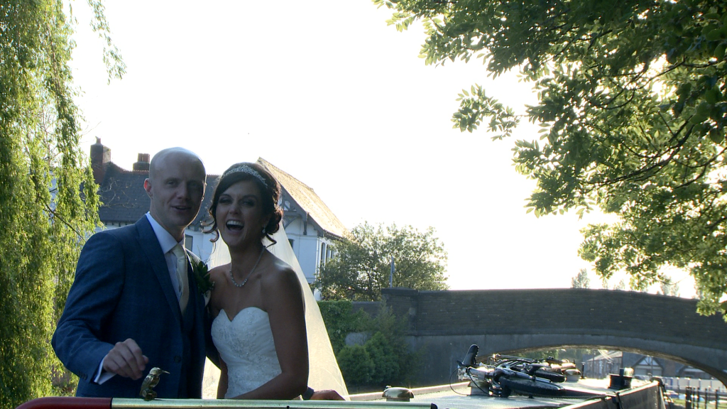 the bride laughs at the wedding videographer as they finish posing on the canal boat by burscough wharf during their wedding reception at The Blue Mallard