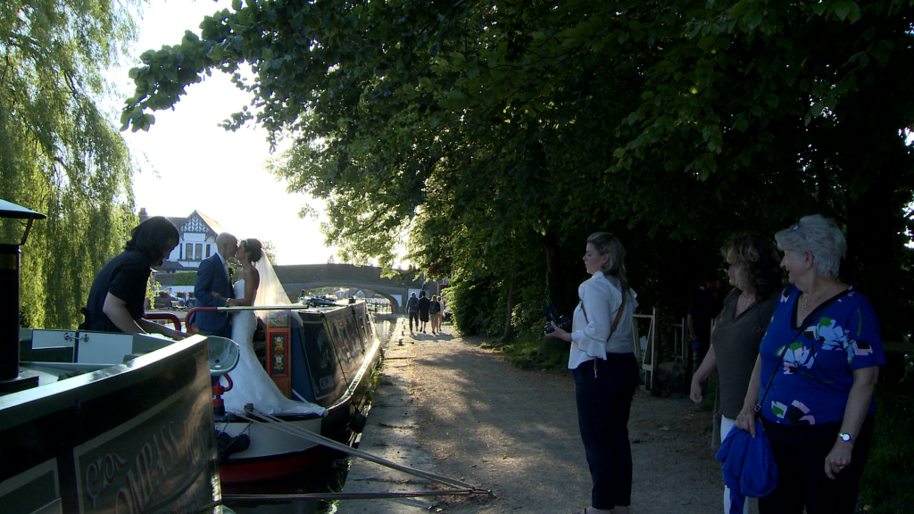 a couple of ladies out walking their dog watch along the leeds liverpool canal as the bride and groom enjoy a few couple portraits on a canal boat near burscough wharf after their wedding breakfast at The Blue Mallard