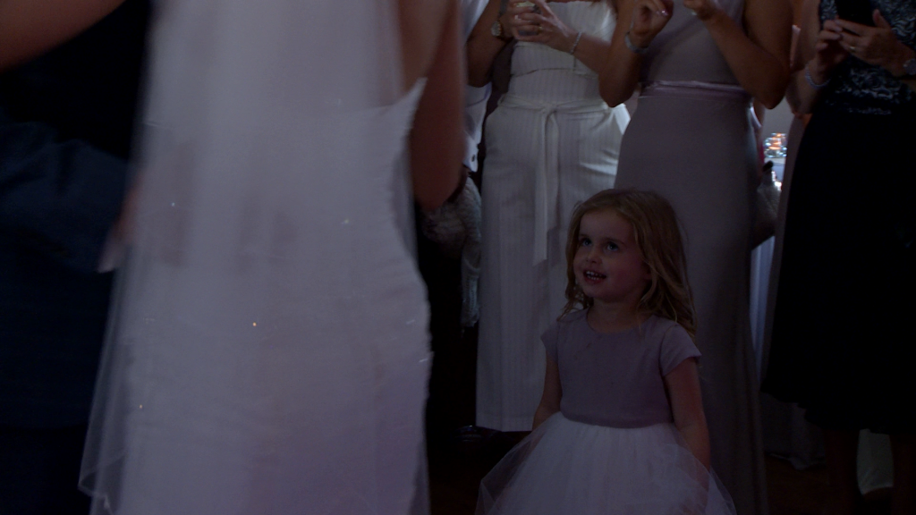 the flower girl smiles up at her mum and dad as the enjoy their first dance as husband and wife at the blue mallard in burscough