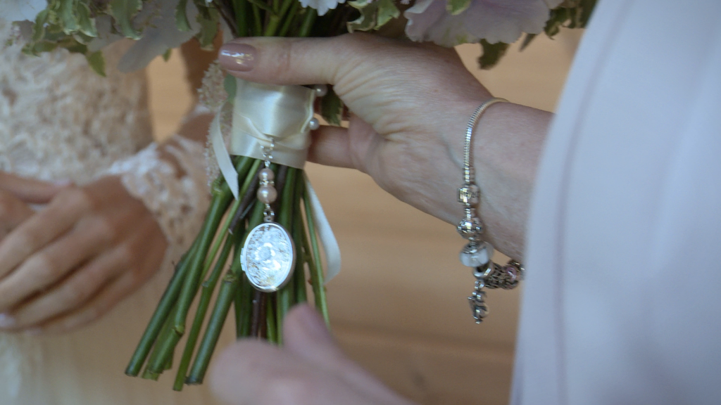 A close up from the wedding video of a memory locket tied to the bridal bouquet ribbon