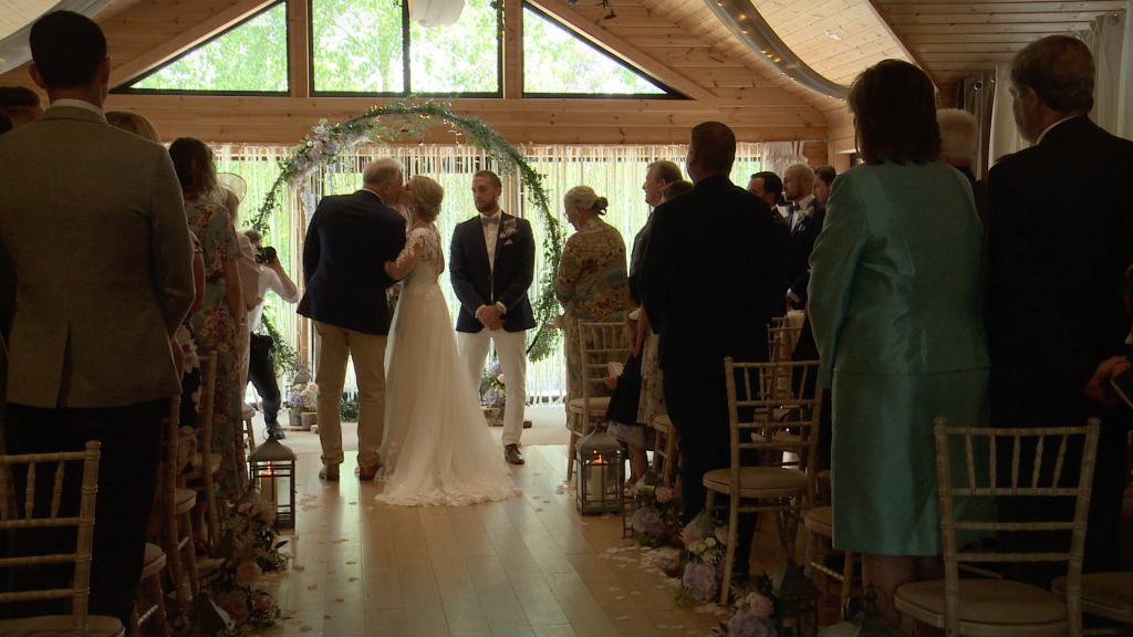 the bride kisses her dad on the cheek. A rustic large floral hoop in the background at their Styal Lodge wedding