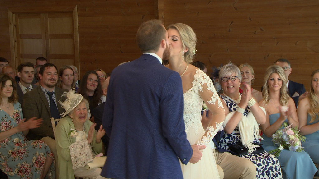 A video of you may kiss the bride and the guests are smiling and clapping behind them at Styal Lodge in Cheshire