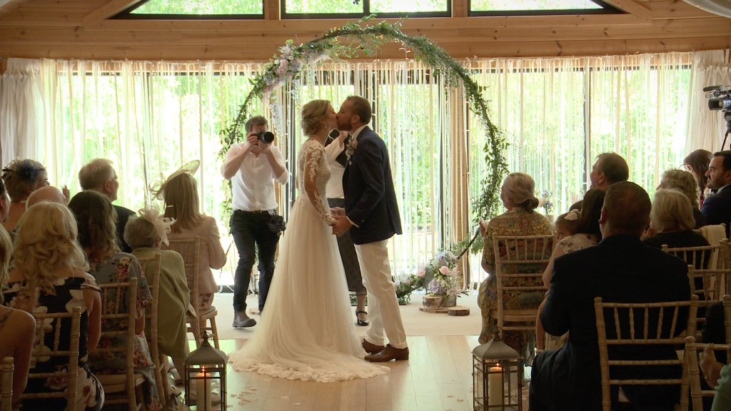 A still from the wedding video of a rustic Styal Lodge wedding with large floral hoop and aisle of white petals