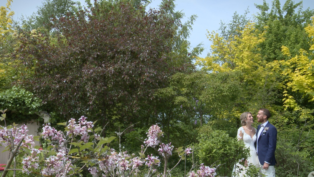 the bride and groom stand amongst bright foliage and purple flowers in the gardens at Styal Lodge in Cheshire