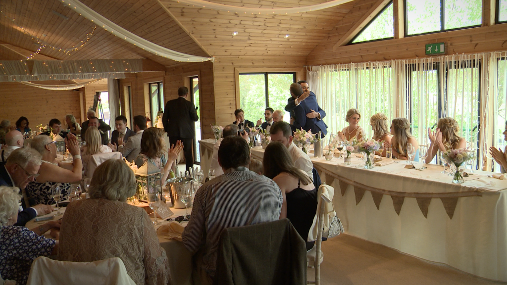 the groom hugs his best man as the rest of the room claps during speeches at Styal Lodge in Cheshire