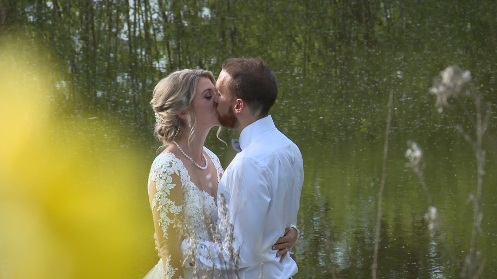a wedding video still of a bride and groom have a kiss on the jetty in front of the lake at Styal Lodge in Cheshire