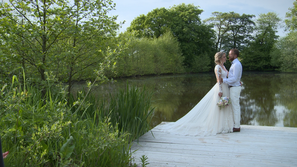 a wider shot of the bride and groom having a chat by the lake Styal Lodge in Cheshire taken from their wedding video